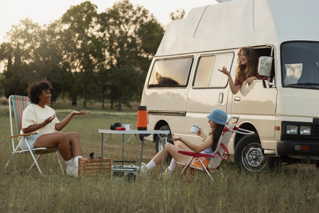 Eine Gruppe von Freundinnen auf Reisen mit einem Vintage-Camper und unterwegs trinken sie etwas Kaffee