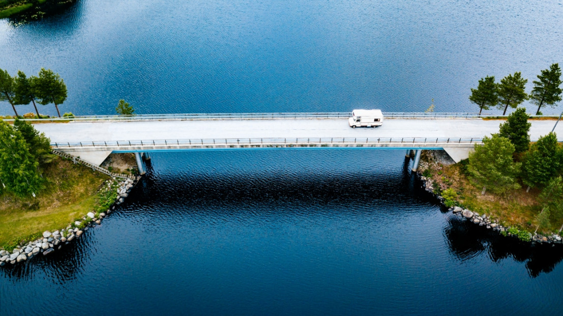 Camper fährt über eine Brücke über einen tiefblauen See.