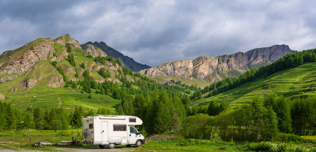 Wohnmobil steht geparkt in einer Umgebung mit vielen Bergen, grünem Gras und einem blauen Himmel