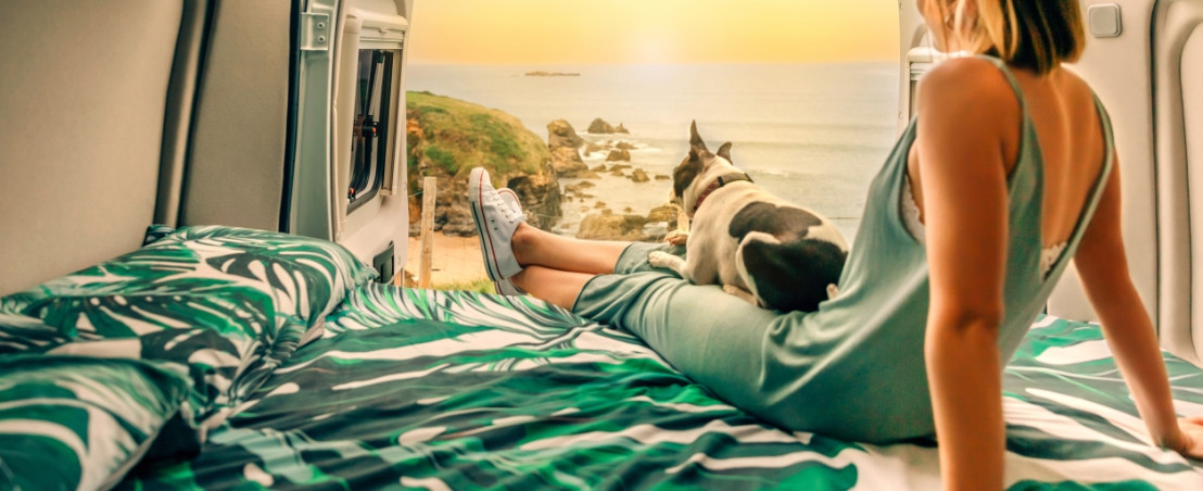 Frau genießt Aussicht vom Camperbett mit Hundchen dabei
