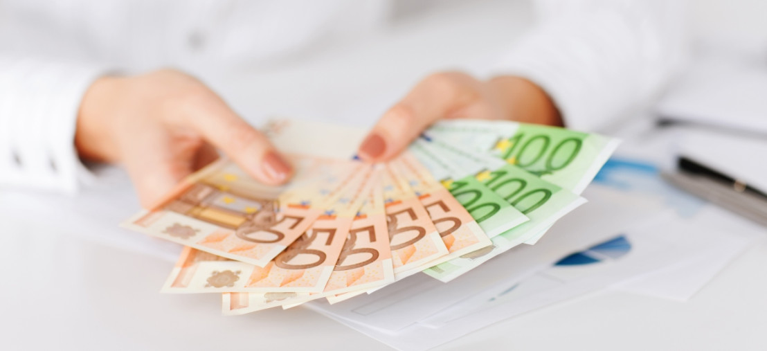 Hände halten Euro-Banknoten, die Einnahmen aus der Campervermietung darstellen.