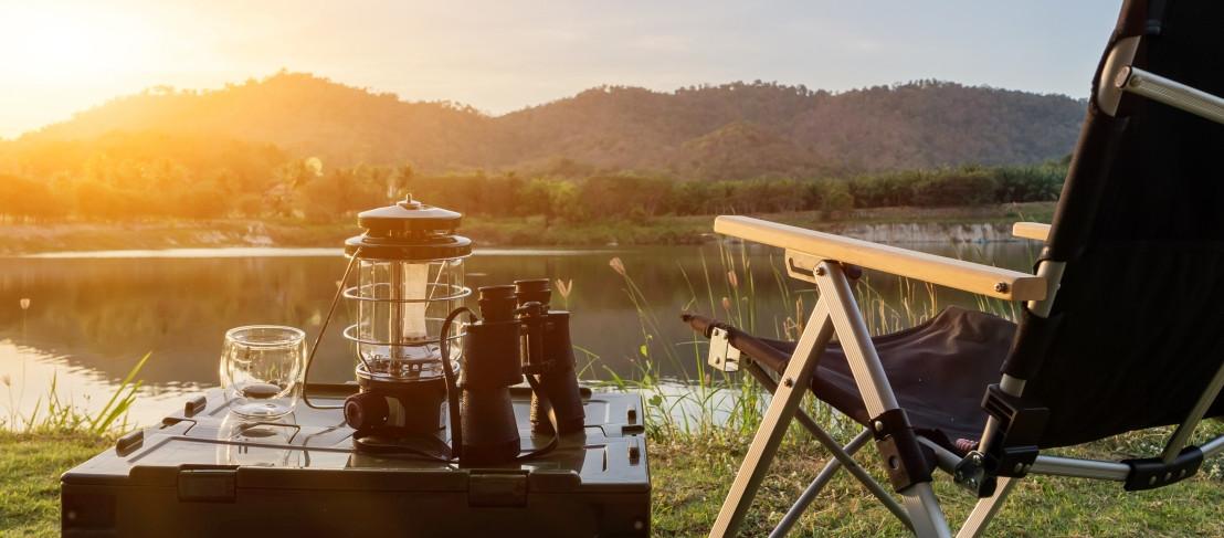 Eine Tasse Kaffee trinken in einem Campingstuhl mit einem wunderschönen Blick auf einen See und Hügel
