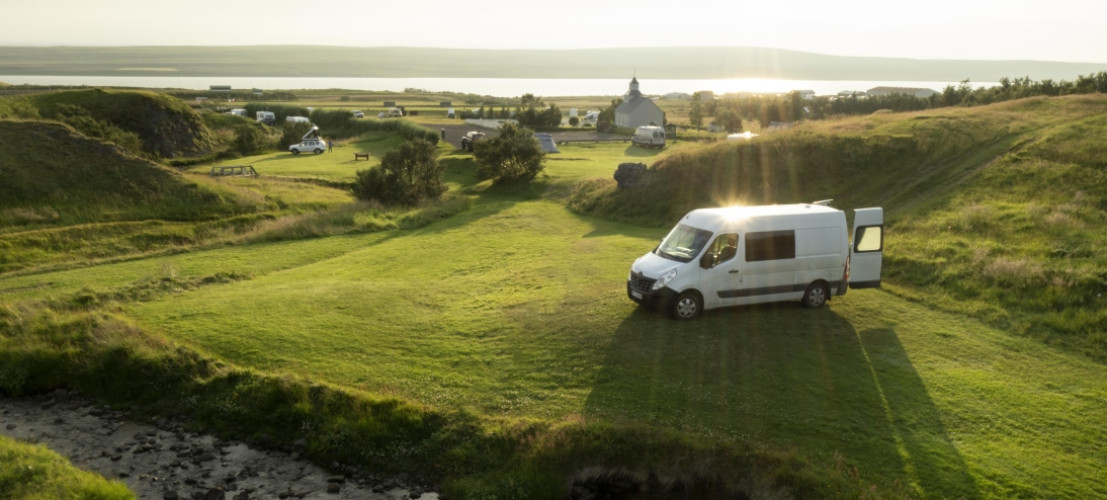 Ein Buscamper geparkt auf einem großen grünen Campingplatz in Island mit prachtvollem Ausblick