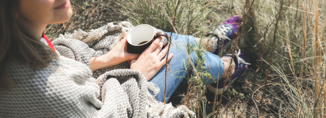 Die Frau trinkt unterwegs mit dem Camper eine Tasse Kaffee im Gras.